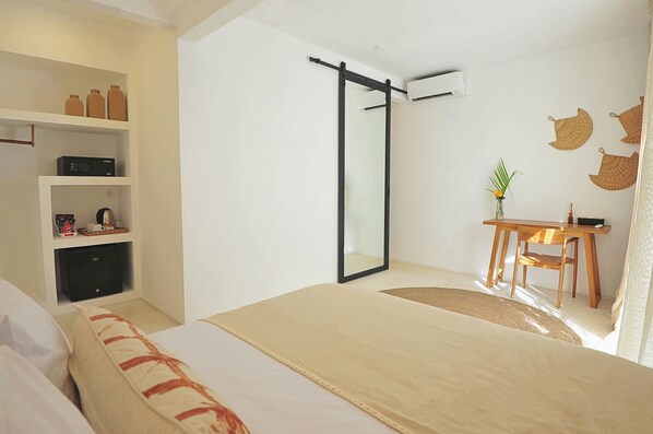 A hotel room with a bed, a desk with a chair, a wardrobe, and a mirror. - Amara Uluwatu (Pecatu)