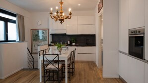 A modern kitchen with white cabinets, a dining table with chairs, a chandelier, and an oven.