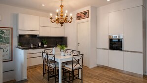 A modern kitchen with white cabinets, a central island with seating, a chandelier, and built-in appliances.