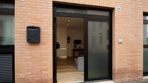 A modern building with a glass door entrance, numbered 27 and 29, leading to an interior with a kitchen and seating area.