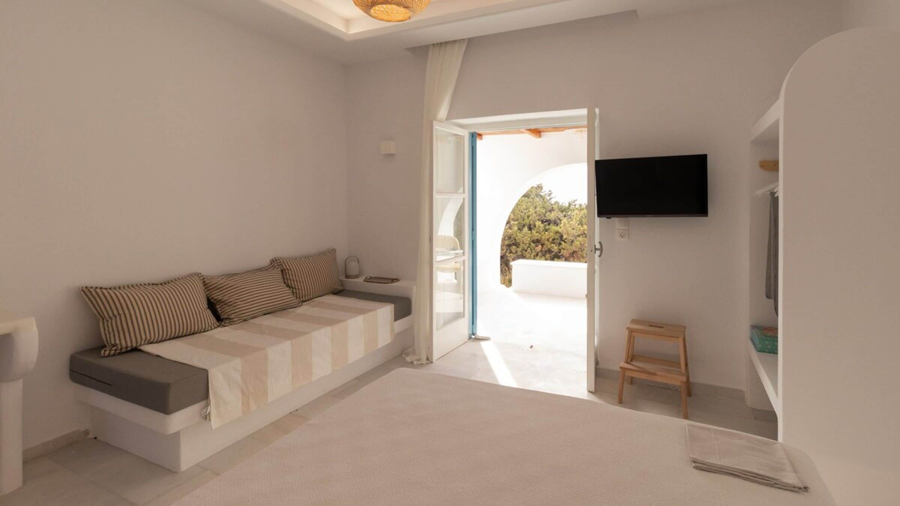 A bedroom with a sofa bed, a TV mounted on the wall, and a small wooden stool.