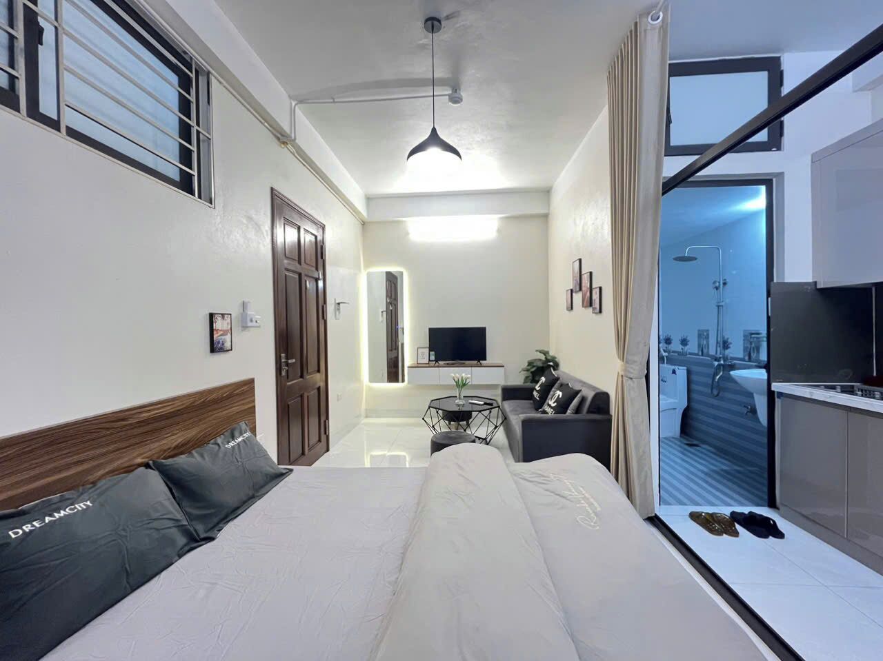 A modern hotel room with a large bed, a sofa, a TV, and a kitchenette.