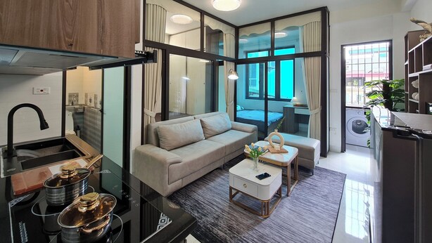 A modern living room with a sofa, coffee table, and kitchen area with pots. - The Little'N Homestay (Hanoi)