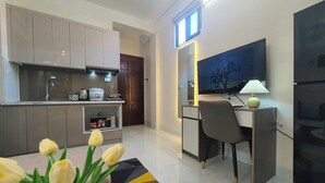 A modern kitchen with a built-in stove, a dining area with a desk and chair, and a large flat-screen TV mounted on the wall. - The Little'N Homestay (Hanoi)