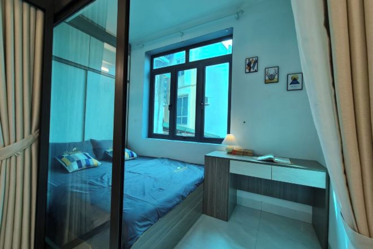 A bedroom with a bed, a desk, and a window.