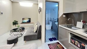 A compact living space with a sofa, coffee table, and a TV in the living area. A kitchen with a sink and countertop is visible. - The Little'N Homestay (Hanoi)