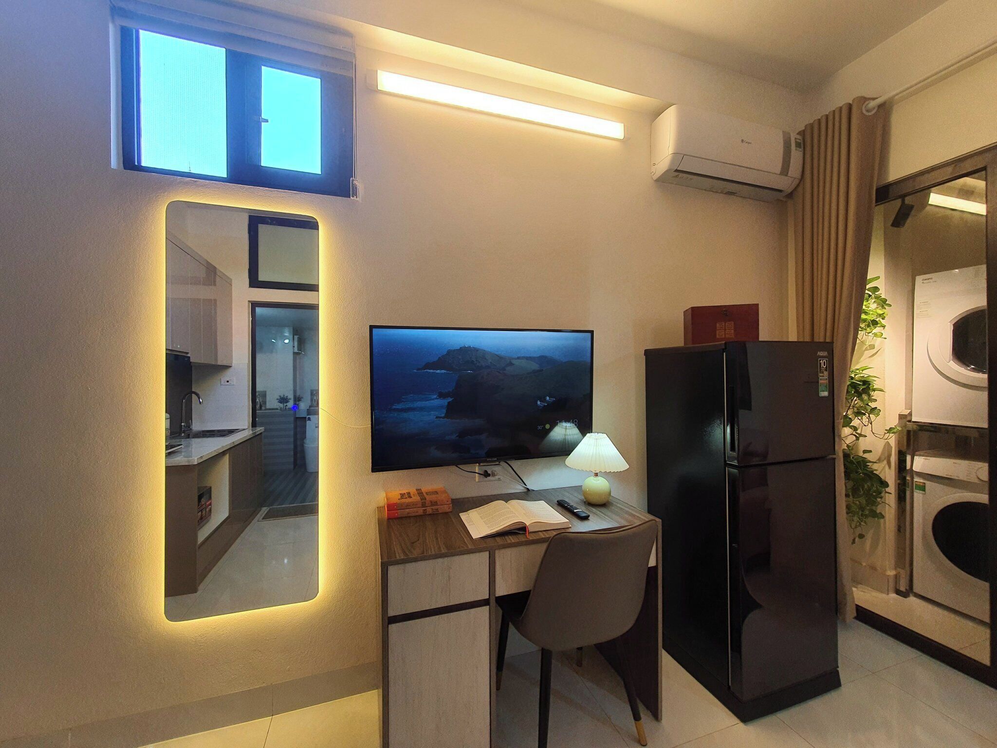 A compact kitchen with a built-in stove, a refrigerator, and a microwave. A flat-screen TV is mounted on the wall above a small dining table with a chair.