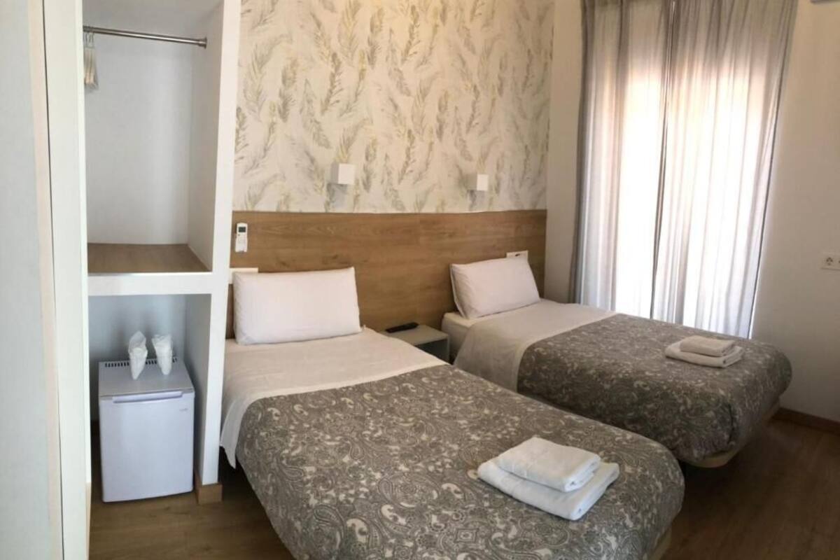 Una habitación de hotel con dos camas, un armario y un refrigerador pequeño.