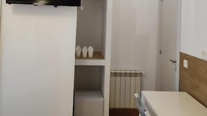Une pièce compacte dotée d’un téléviseur à écran plat fixé au mur, d’une petite table blanche et d’un meuble de rangement intégré avec des étagères.