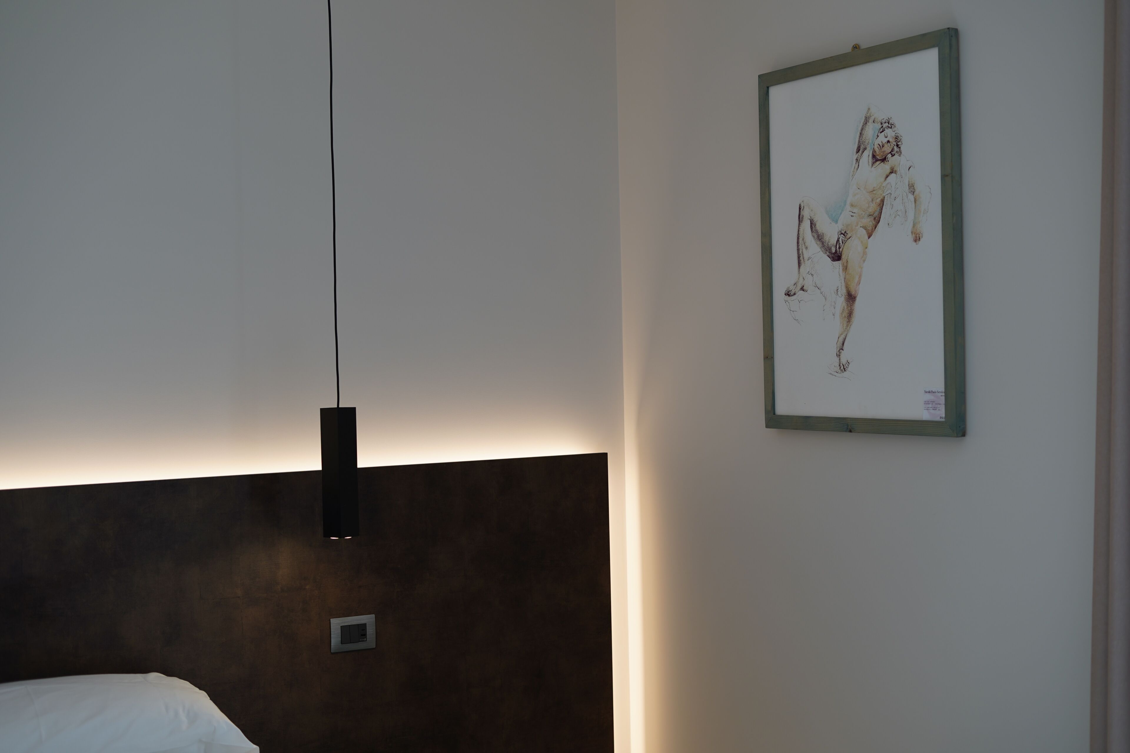 Una habitación de hotel moderna con una cama grande, una lámpara de pared y una obra de arte enmarcada.