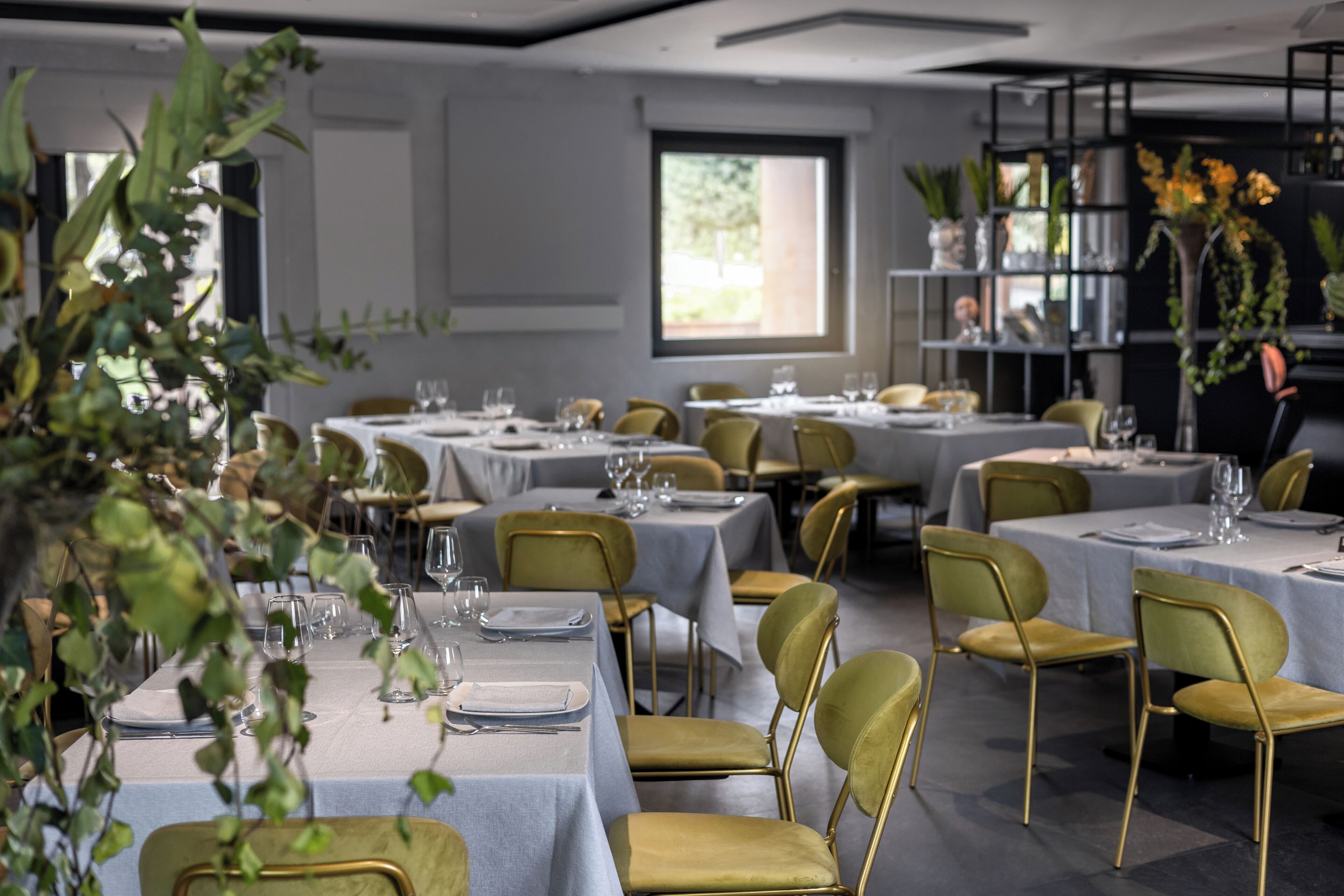A dining area with tables set for service, chairs, and a large window providing natural light.