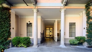 Fachada de edificio con columnas, puerta con reja y plantas en macetas.