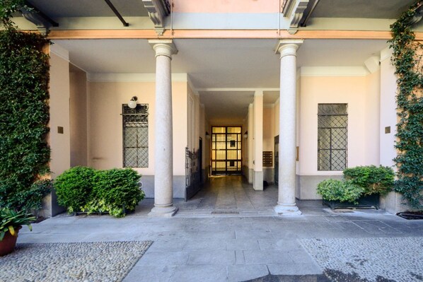 A building entrance with columns, a gated door, and potted plants.