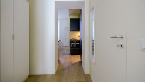 Un pasillo que conduce a una cocina con suelo de madera y paredes blancas.