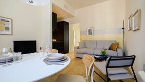 Una sala de estar moderna con un sofá, una mesa de comedor con sillas, un televisor y una planta.