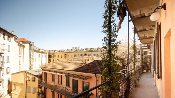 Un balcón estrecho con baranda metálica, con vistas a una hilera de edificios de diversos estilos arquitectónicos.