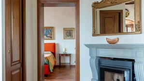 Une pièce avec une porte en bois, une cheminée, un lit recouvert d’une couverture colorée et deux tableaux encadrés accrochés au mur.