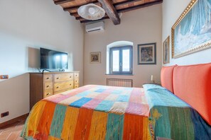 Une chambre à coucher avec un lit, une télévision, une commode, une fenêtre et un tableau accroché au mur.