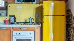 Une cuisine avec des carreaux de céramique jaunes, un réfrigérateur jaune, des armoires en bois, une cuisinière à gaz et un four à micro-ondes.