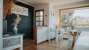 A room with a wooden floor, a white table with chairs, a window with a view of trees, and a door with a window. - Spindrift Falmouth, adventurers coastal haven (Break O'Day)