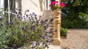 A building with a stone staircase and a flower bed with purple flowers. - MANOIR LE COUTUREAU (Rouffignac-de-Sigoulès)
