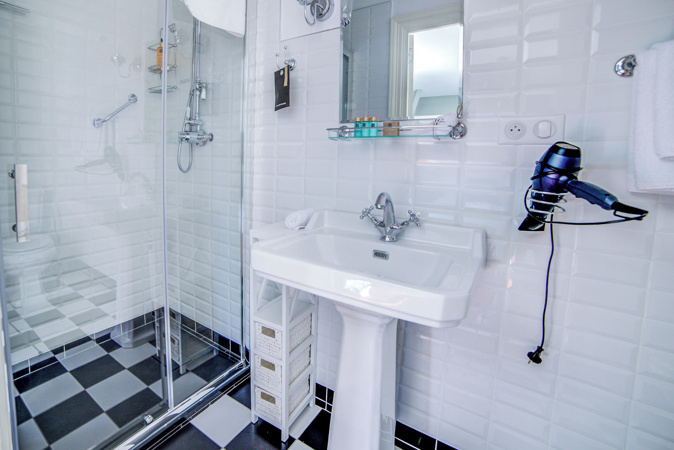 A modern bathroom with a glass shower enclosure, a white sink, and a hairdryer mounted on the wall.