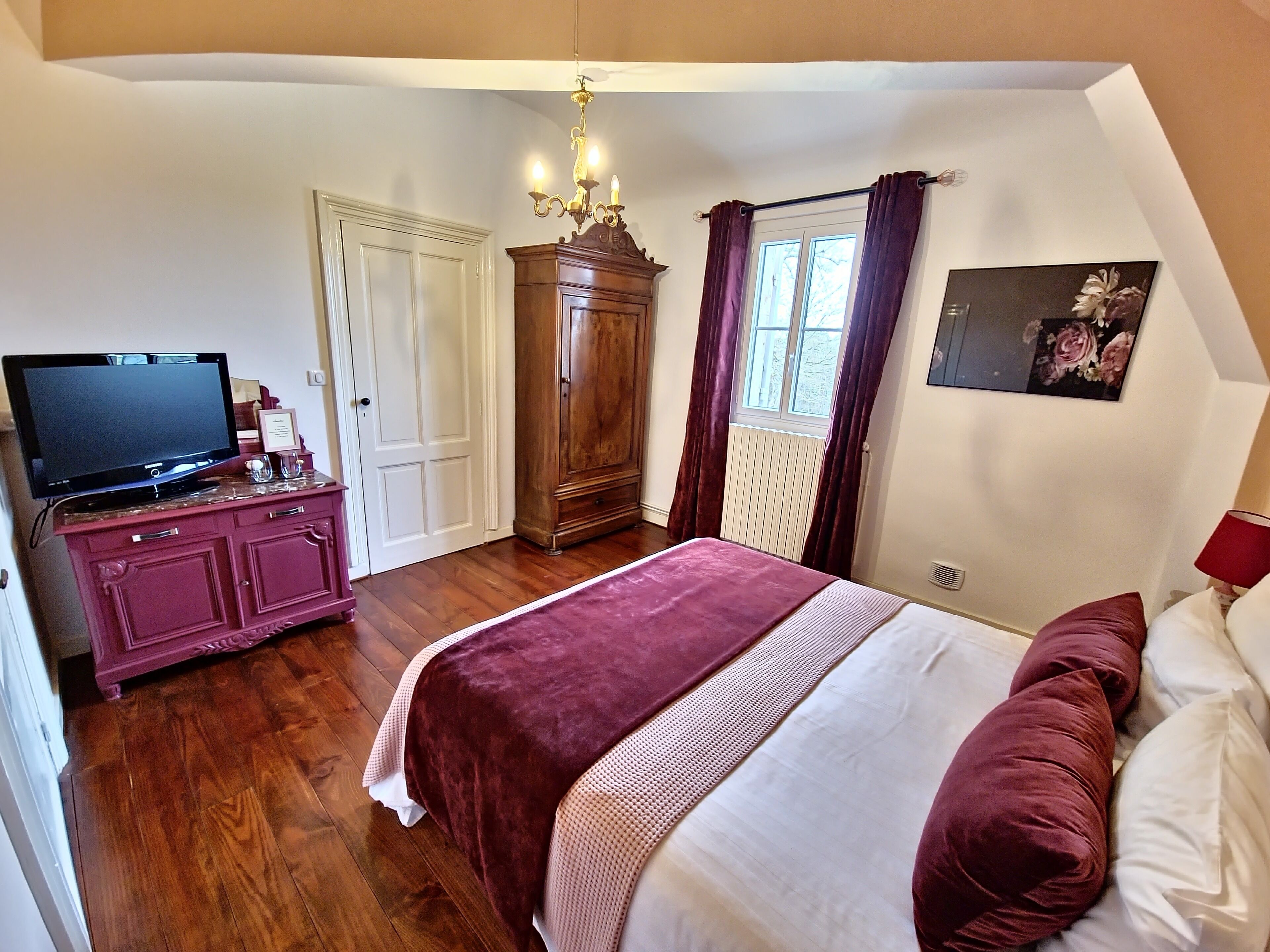 Un dormitorio con cama, televisor en una cómoda, armario y ventana con cortinas.