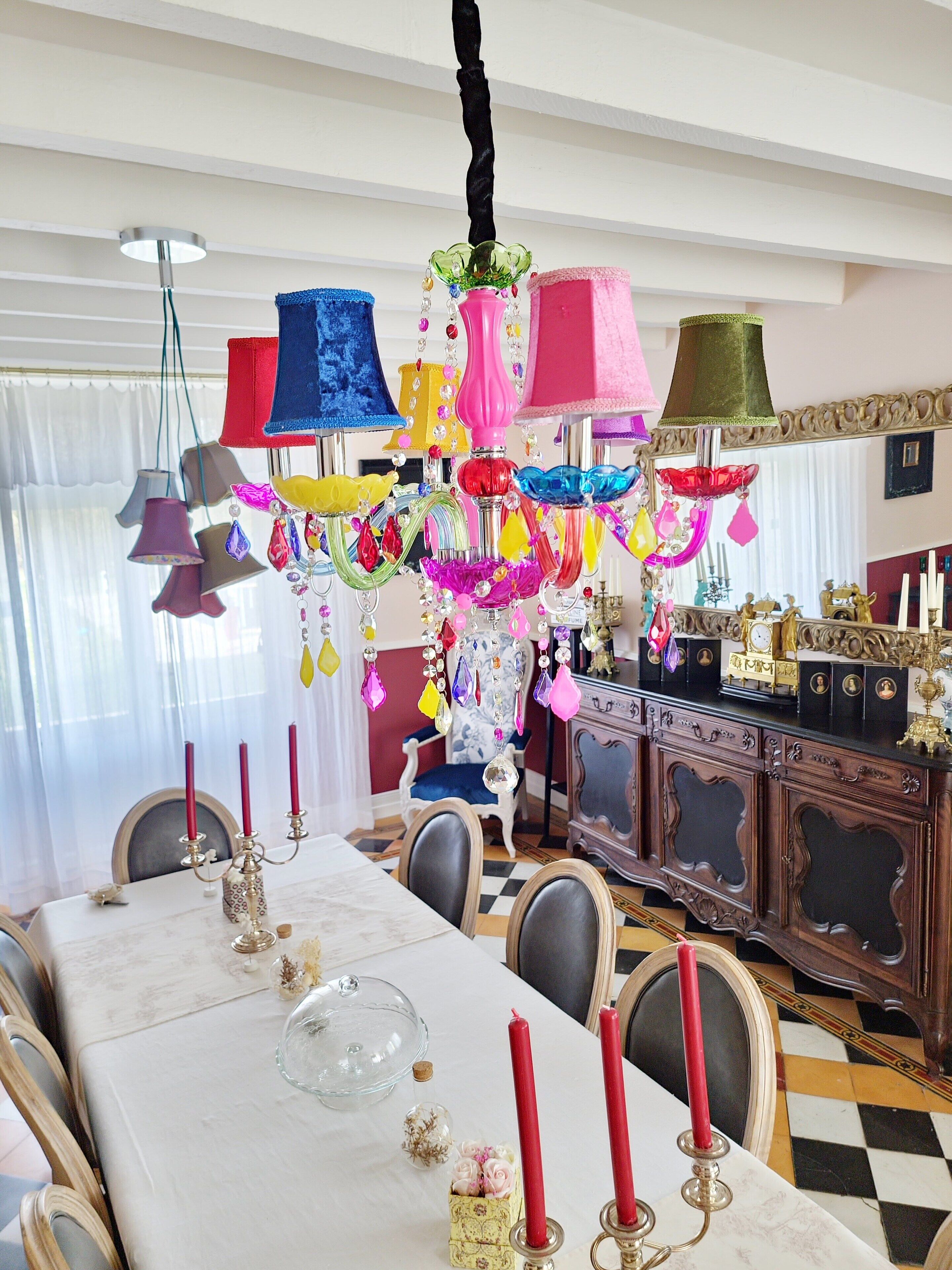 Un coin repas agrémenté d’un lustre, d’une table décorée de bougies et d’un miroir placé au-dessus de la table.