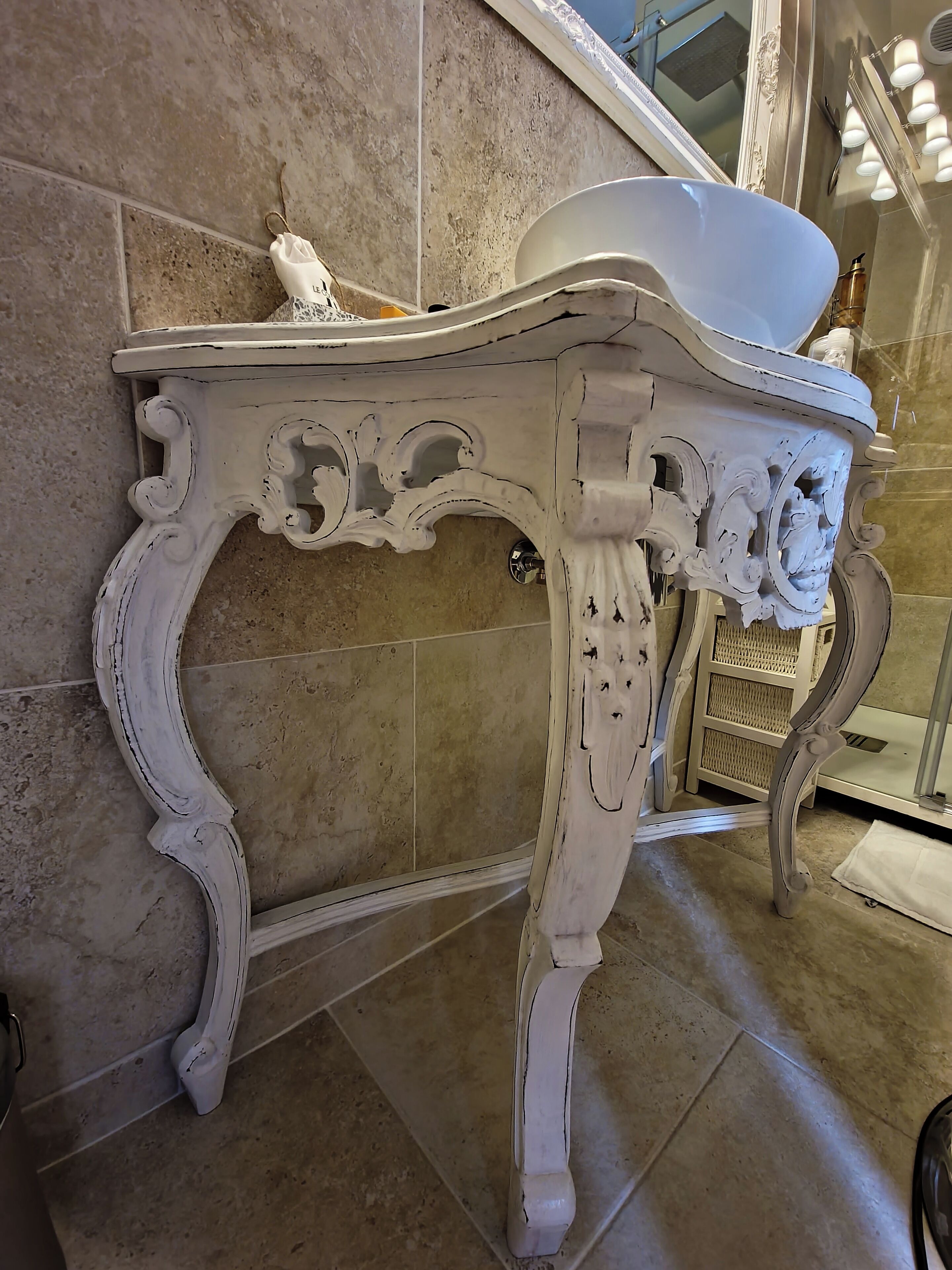 A white ornate table with a basin, positioned against a tiled wall.