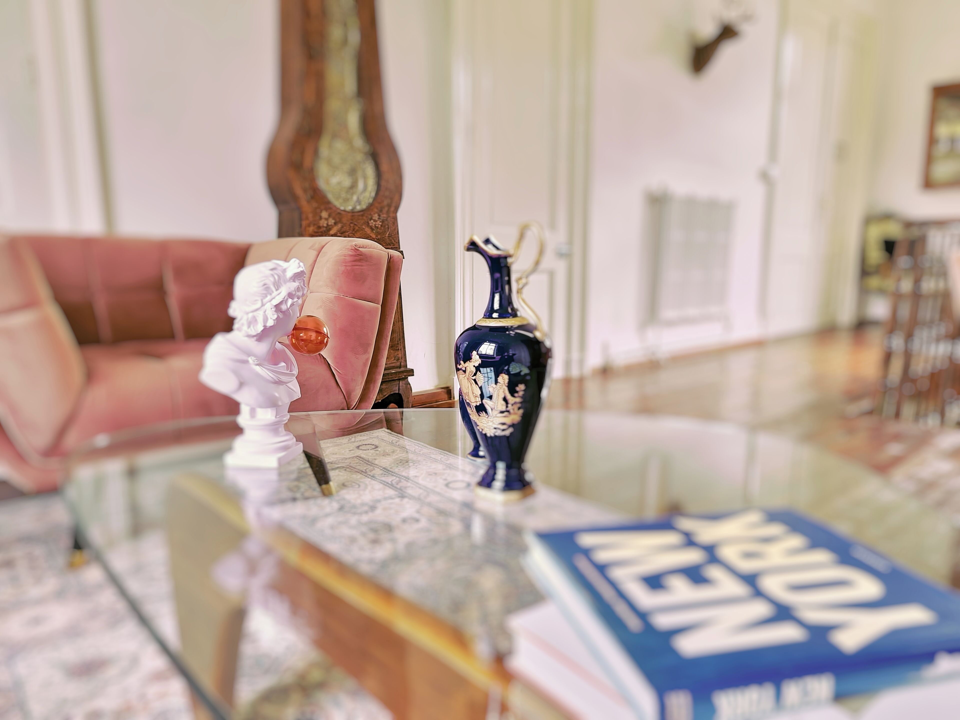 Une table basse en verre sur laquelle sont posés un livre sur New York, une statuette blanche et un vase bleu agrémenté de motifs dorés.