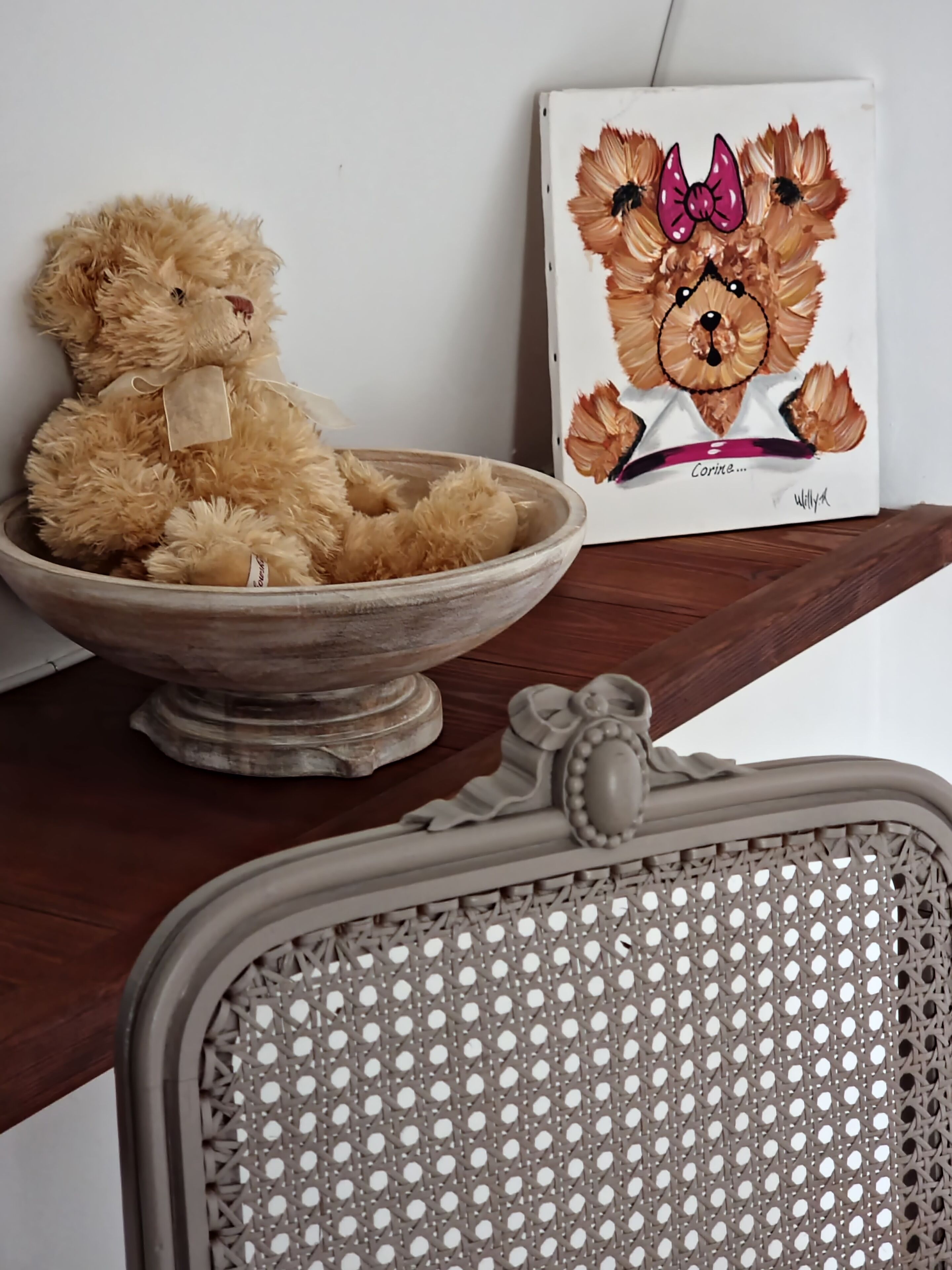 Un bol en bois avec un ours en peluche, un portrait encadré d’un chien et une chaise en osier.