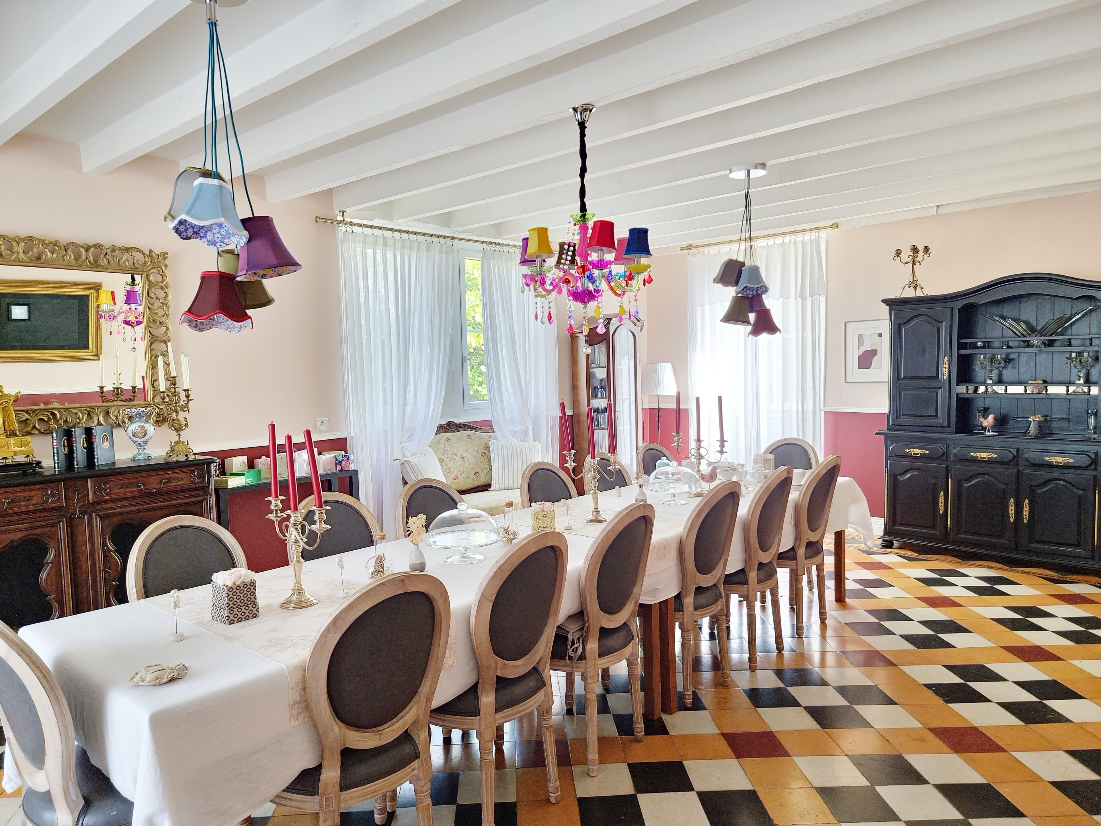 Une salle à manger avec un sol à carreaux, une longue table dressée pour six personnes et un lustre.
