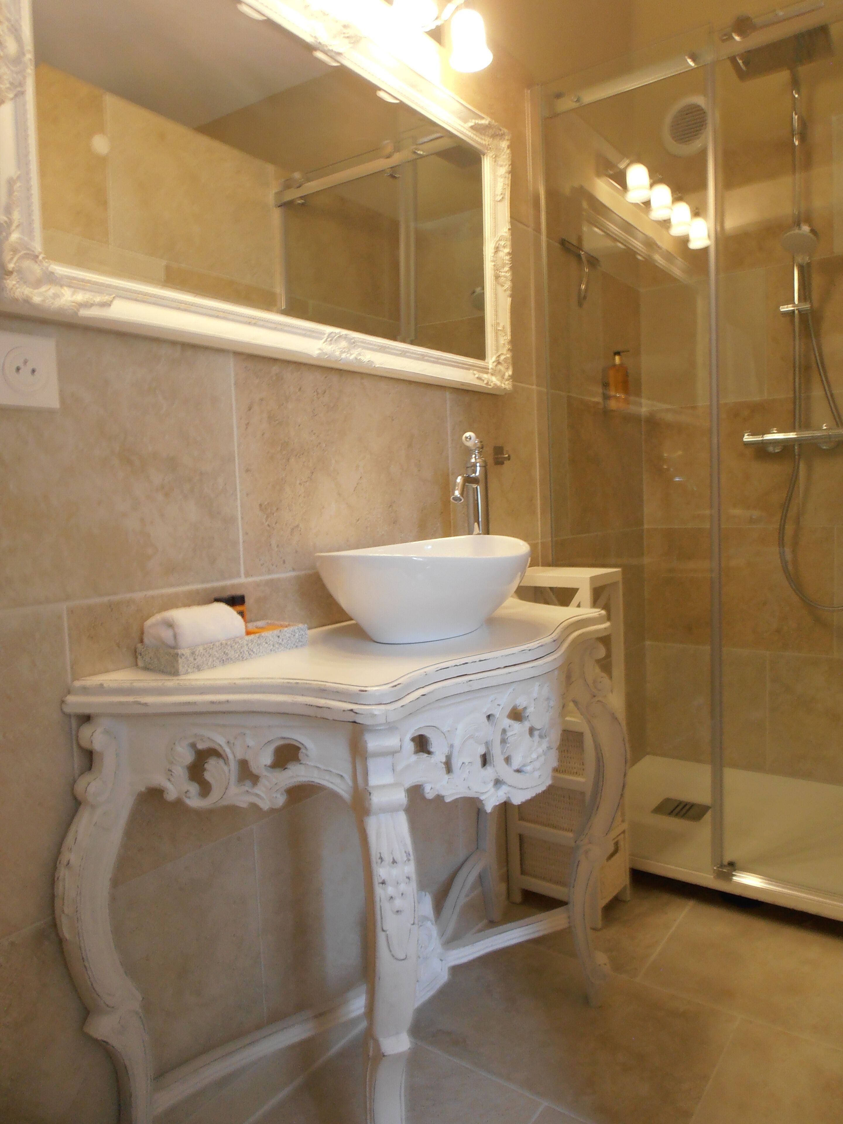 Un baño con tocador blanco, un espejo grande y zona de ducha con mampara de vidrio.