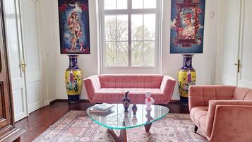 A room with a pink sofa, a glass coffee table, and two vases on either side of a window.