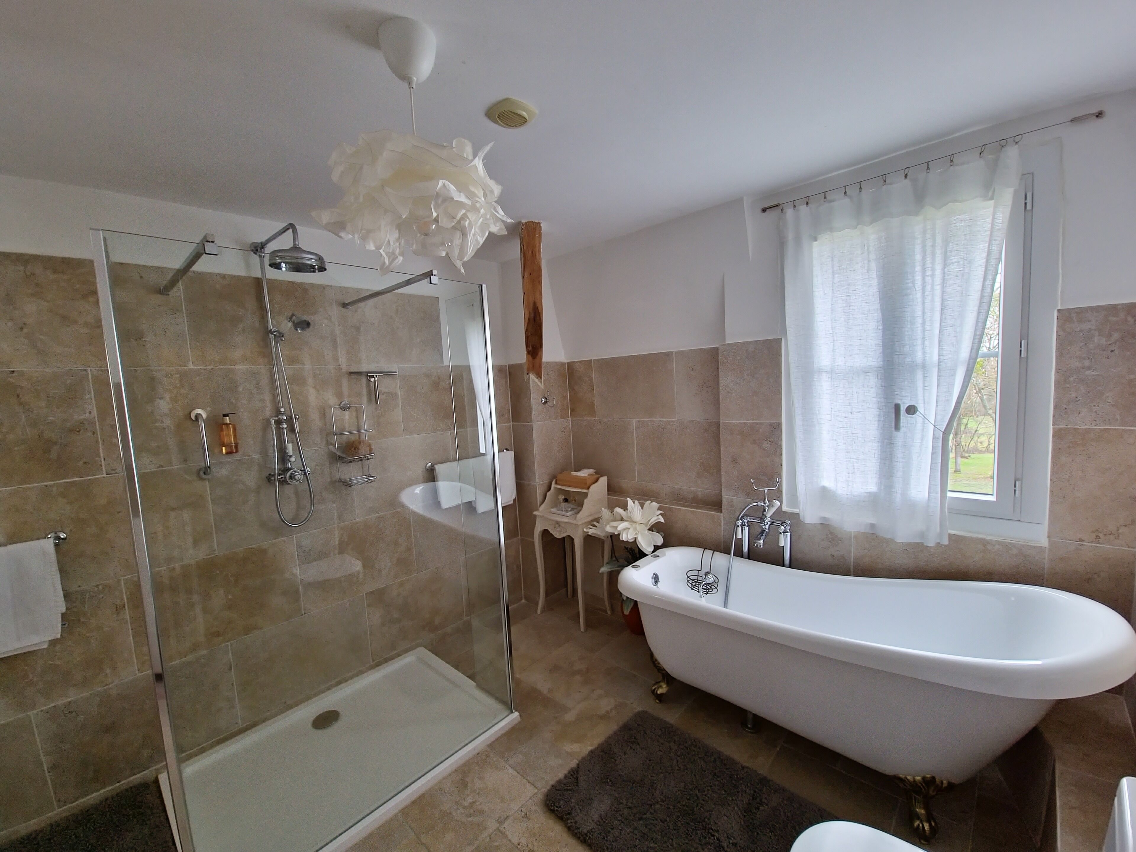 Un baño con ducha envuelta en vidrio, una bañera independiente y un ventanal con vistas.