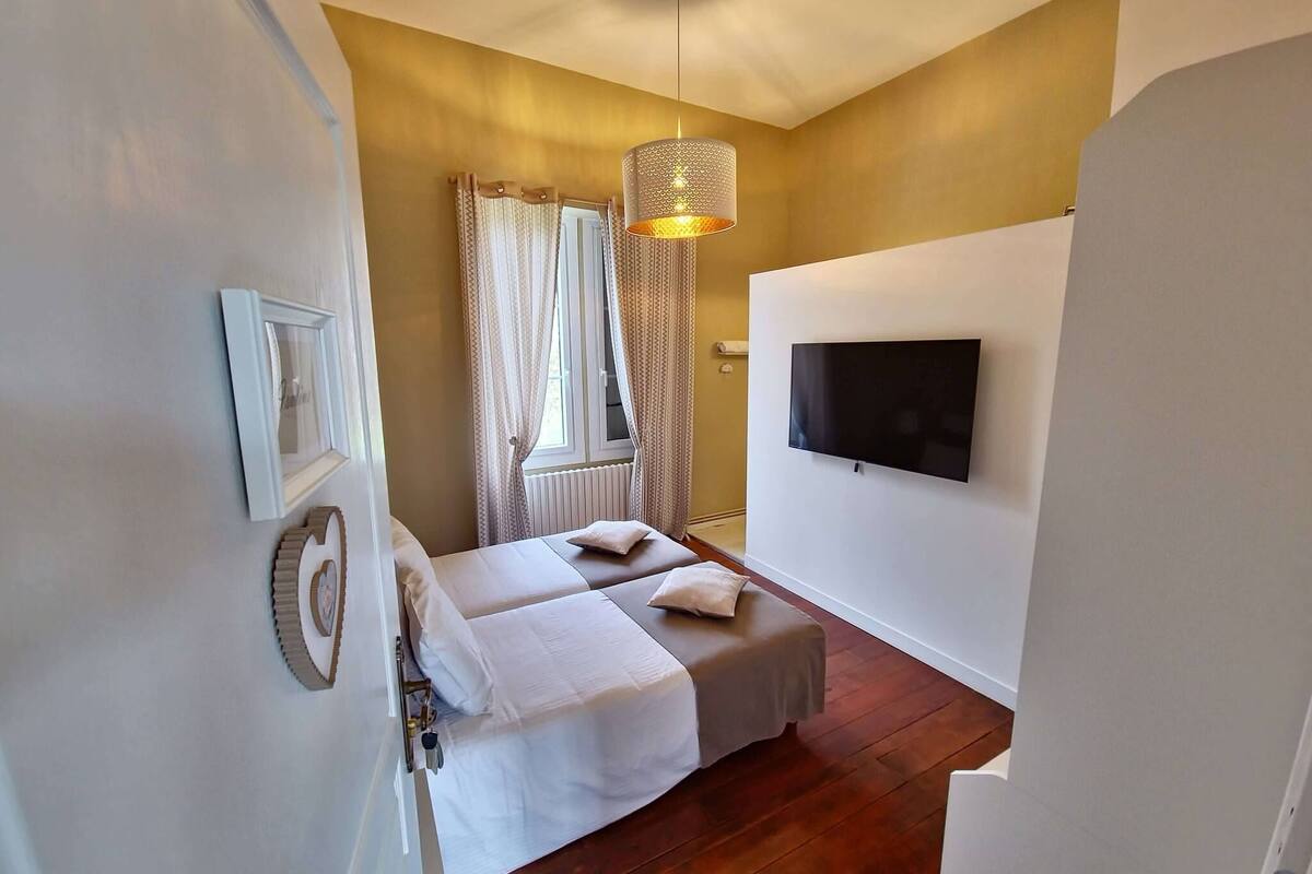 Camera da letto con due letti, una televisione a parete e una finestra con tende.