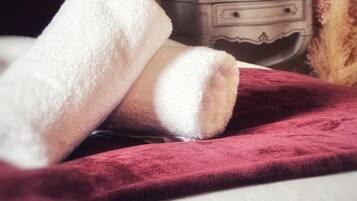 A bed with a white blanket and a red throw, a nightstand with a vase, and a wall with a door in the background.