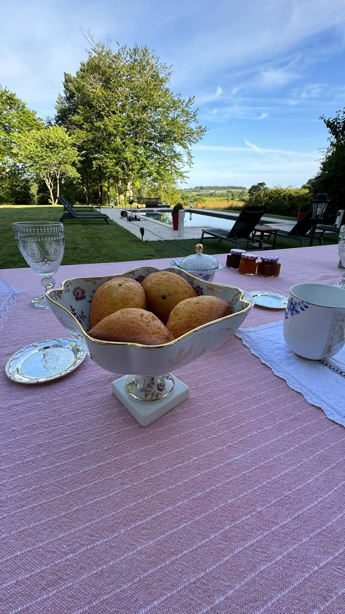 Una mesa con un bol de pan estampado con motivos florales, un vaso y una tetera sobre un mantel rosa.