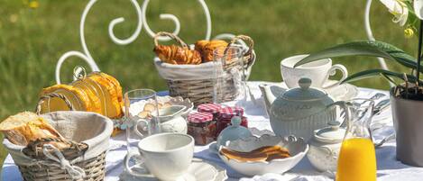 A picnic setup with bread, pastries, cups, and a jug of juice on a white tablecloth.