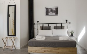 Ein modernes Schlafzimmer mit einem Bett auf Podest, einem großen Spiegel, einem gerahmten Foto an der Wand und einem kleinen Nachttisch mit Pflanze.