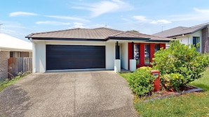 A residential house with a garage, a driveway, and a well-maintained garden. - Coomera Family Home - Sleeps up to 8 People (Coomera)