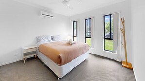 A modern bedroom with a bed, a nightstand, a ceiling fan, and large windows. - Coomera Family Home - Sleeps up to 8 People (Coomera)