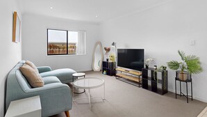 A modern living room with a sofa, TV, and decorative plants. - Coomera Family Home - Sleeps up to 8 People (Coomera)