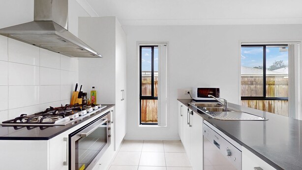 A modern kitchen with a gas stove, oven, and a microwave. There are two windows providing natural light and a view of the outside. - Coomera Family Home - Sleeps up to 8 People (Coomera)