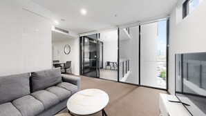 A modern living room with a grey sofa, a white coffee table, and a TV on a white cabinet.