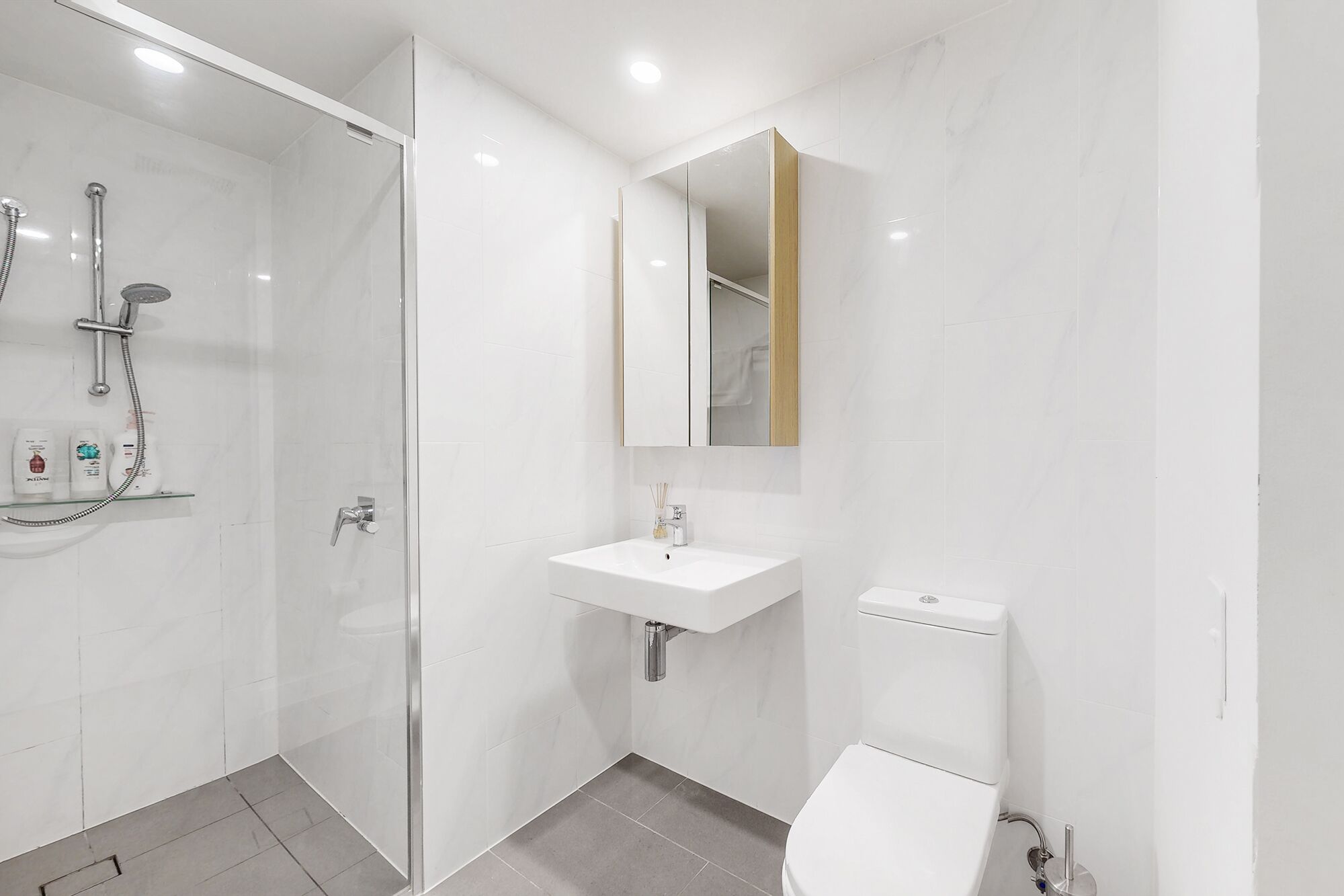 Un baño moderno con ducha de vidrio, lavamanos blanco y un inodoro.