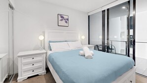 A modern bedroom with a bed, bedside tables, a nightstand, a framed picture, and a view of the outside.