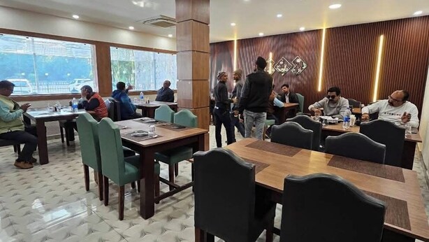 Ένα εστιατόριο με εξαγωνικό μοτίβο στο δάπεδο, ξύλινα τραπέζια και καρέκλες, καθώς και μεγάλα παράθυρα που προσφέρουν θέα.