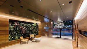 A modern lobby with a wooden wall, a green vertical garden, and a seating area with two chairs and a small table.