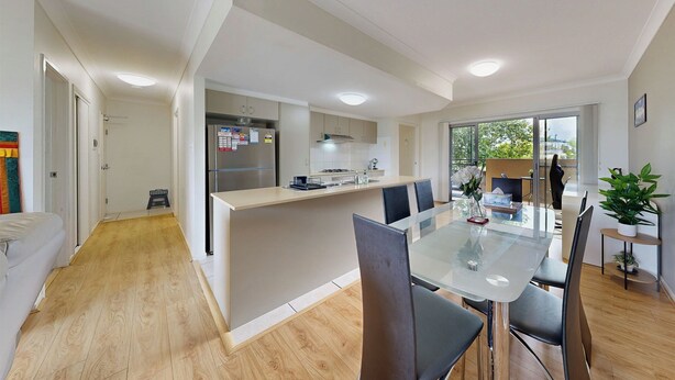 Una cocina moderna con una isla central, un comedor con mesa de vidrio y vistas al exterior.